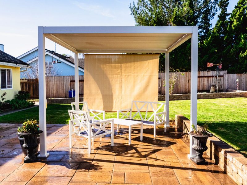 Spacious backyard patio and pergola installation in Santa Maria featuring textured pavers, lawn, and raised retaining walls.