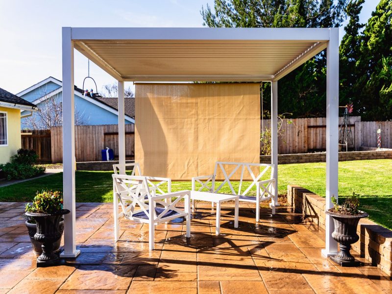 Modern white pergola installed over a custom paver patio with outdoor seating area in a Santa Maria backyard.