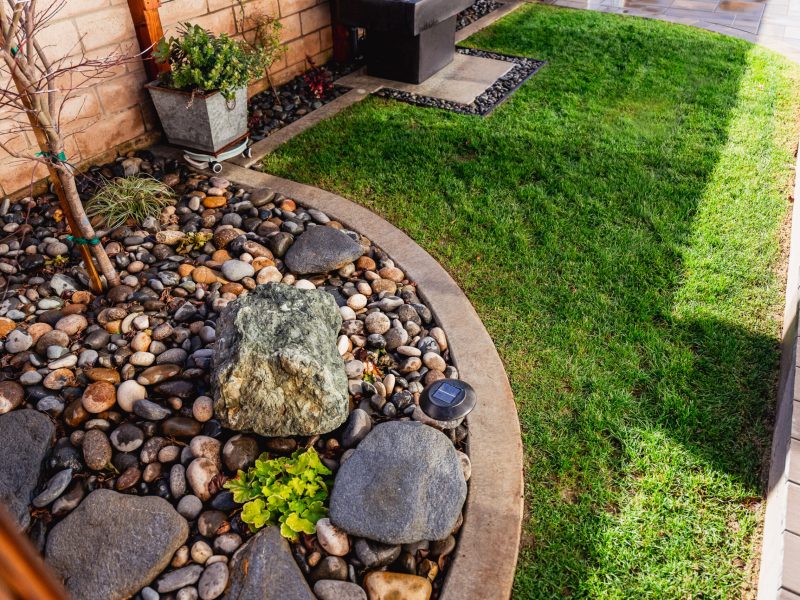 Decorative river rock planting bed with curved concrete edging in a Santa Maria side yard.