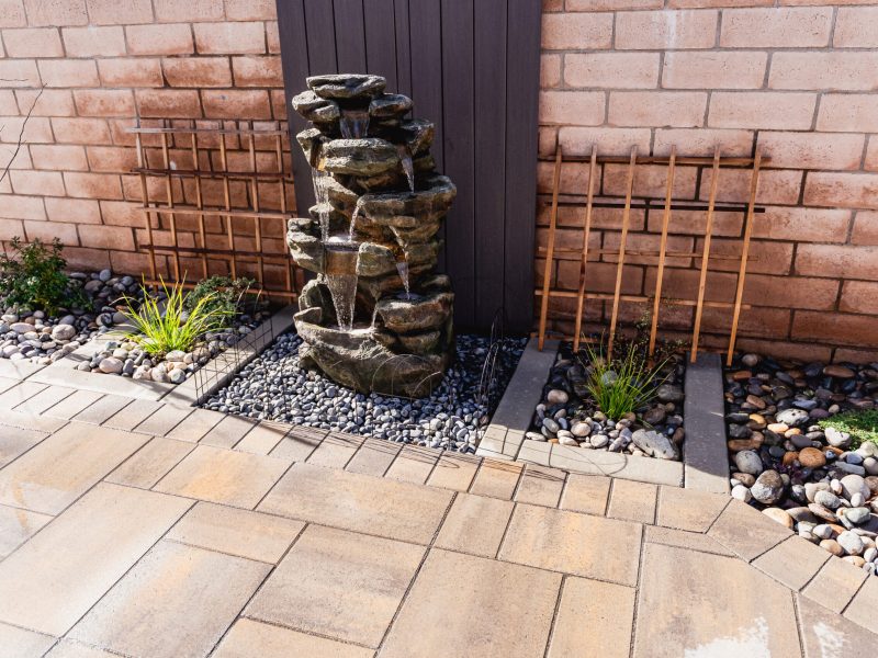 Stacked stone waterfall fountain surrounded by river rock and pavers in Santa Maria.