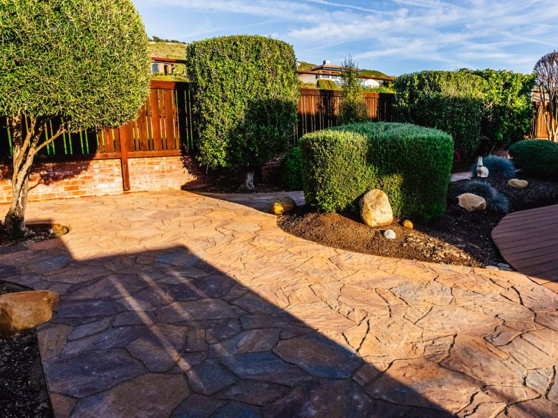 Custom stamped concrete walkway integrated with landscaped shrubs and decorative boulders in Shell Beach.
