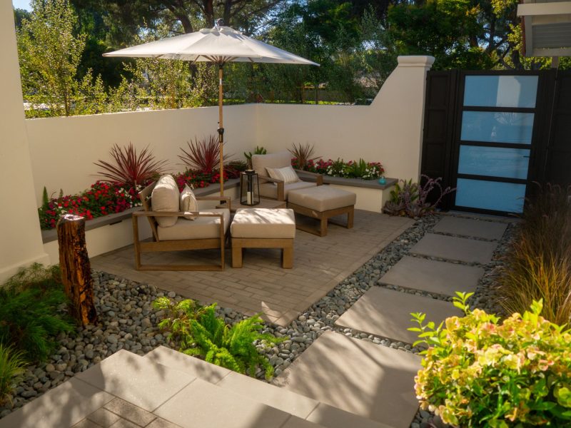 Compact backyard lounge space with patio chairs, planters, and stepping stone walkway in a modern landscape.