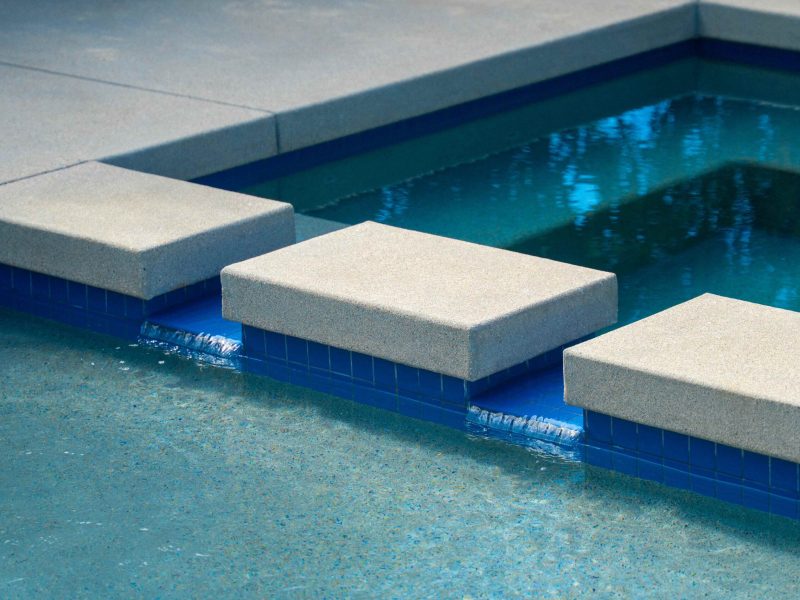 Close-up of square stepping pads leading across a spa and swimming pool with blue tile interior.