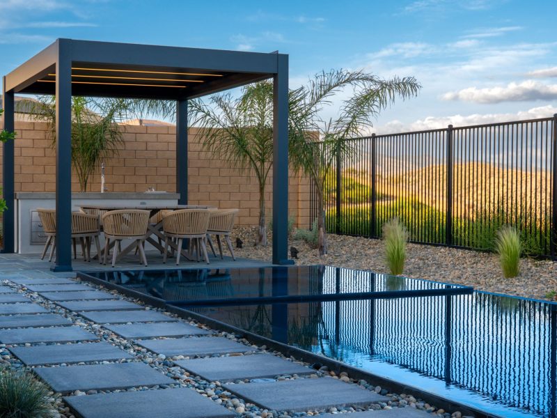 Geometric concrete stepping stones set in river rock running parallel to narrow zero-edge pool in contemporary minimalist landscape.