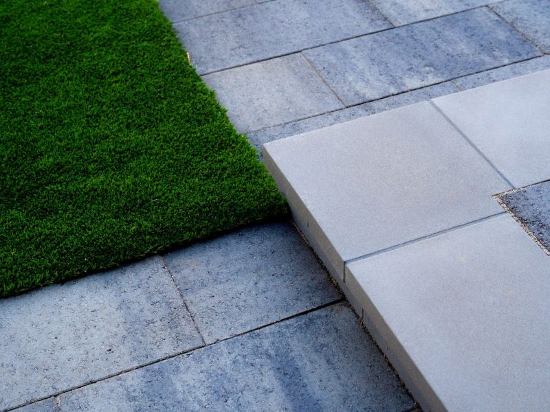Clean transition step between artificial turf and stone paver patio in a contemporary outdoor design.